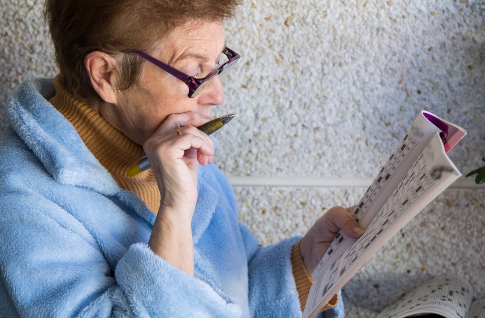 An older adult woman in her sweater solving a crossword puzzle.