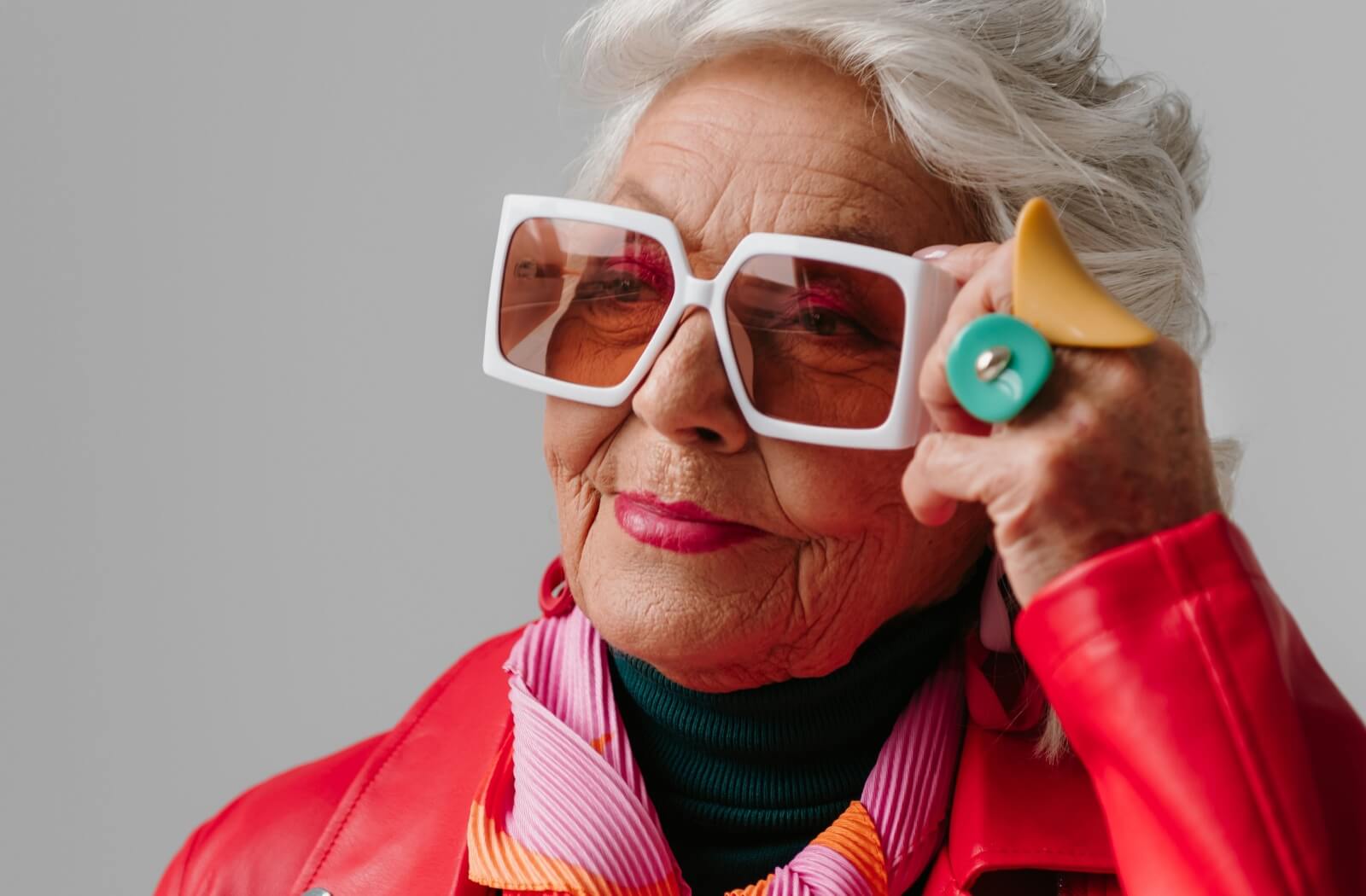 A stylishly dressed older adult adjusts their bold sunglasses.