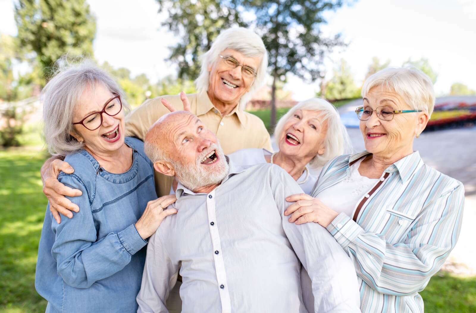 A lively group of older adult friends gather closely, sharing laughter and a playful moment.