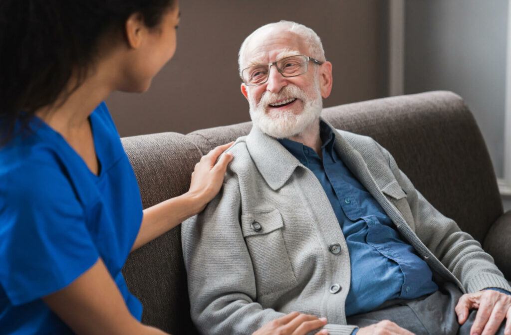 An older adult in a senior living community sitting on a couch, smiling and having a conversation with a caregiver